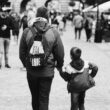 Father and son holding hands while walking through a busy city street in grayscale.