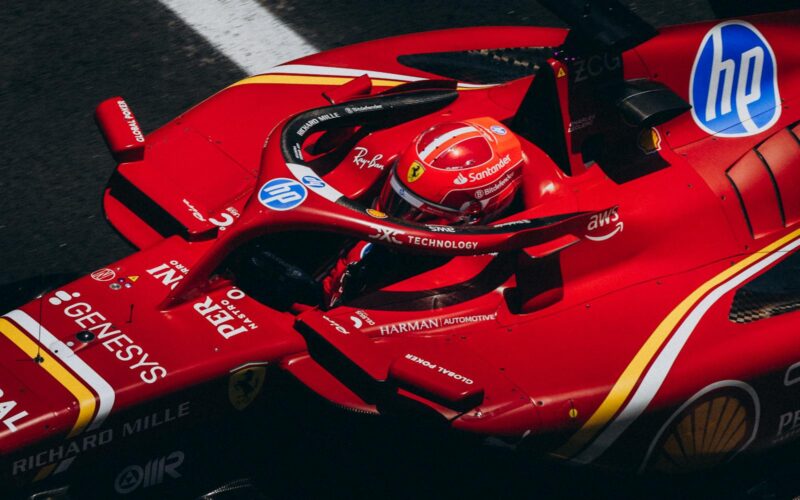 High-speed red racing car zooming down the track, showcasing logos and driver focus.