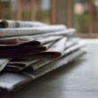 A close-up of a stack of newspapers resting on a desk, symbolizing information and media.