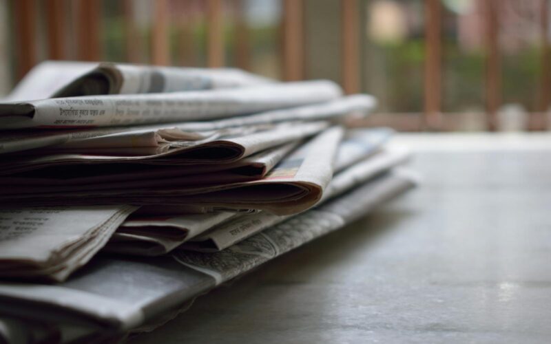 A close-up of a stack of newspapers resting on a desk, symbolizing information and media.