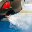 A close view of a car's exhaust pipe emitting smoke on a sunny day, highlighting pollution.