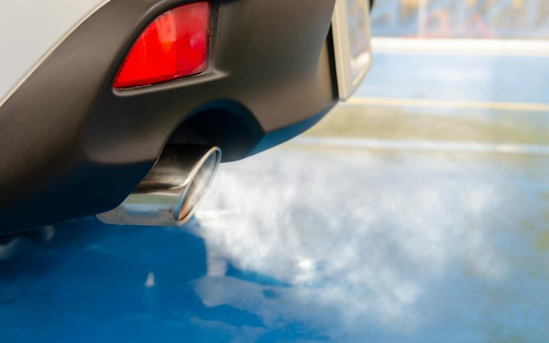 A close view of a car's exhaust pipe emitting smoke on a sunny day, highlighting pollution.