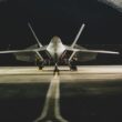 A Lockheed Martin F-22 Raptor jet parked symmetrically in a hangar at night.