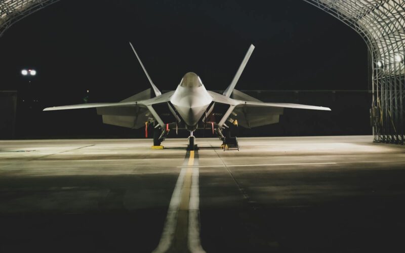 A Lockheed Martin F-22 Raptor jet parked symmetrically in a hangar at night.