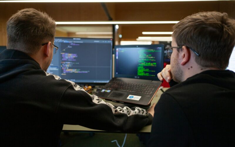 two men sitting in front of a laptop computer