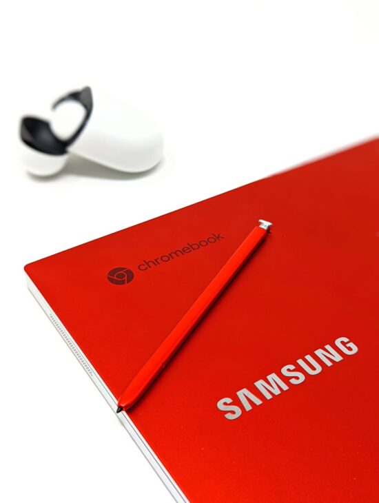 A sleek red Samsung Chromebook with a stylus and earbuds on a white background for a modern tech vibe.