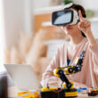inovatie o femeie poarta un headset vr si are un brat robotic pe birou