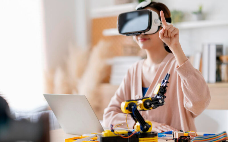 inovatie o femeie poarta un headset vr si are un brat robotic pe birou