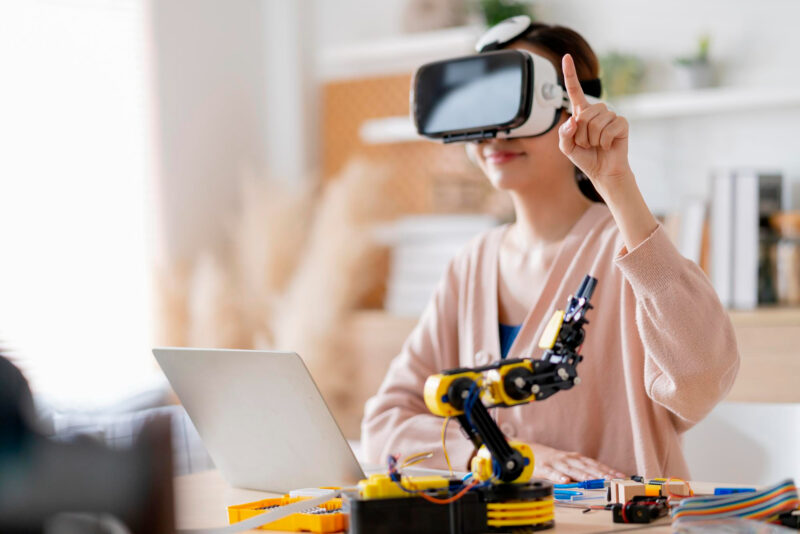 inovatie o femeie poarta un headset vr si are un brat robotic pe birou