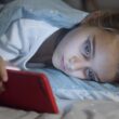 Un copil stând pe telefon în pat
