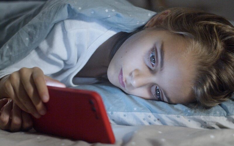 Un copil stând pe telefon în pat