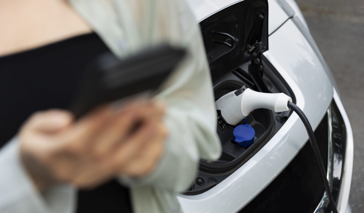 o femeie foloseste telefonul la o statie de incarcare pentru masini electrice