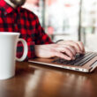 un barbat foloseste un laptop alaturi de care are o cana de cafea