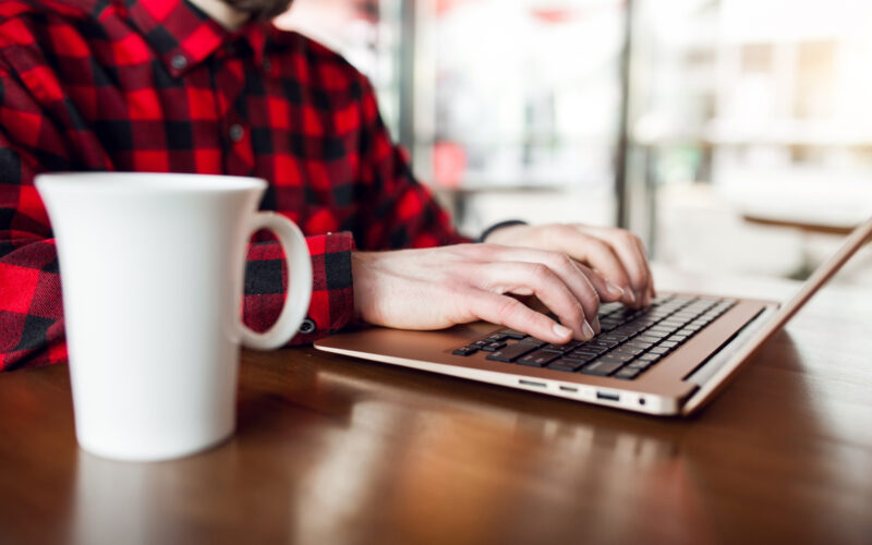 un barbat foloseste un laptop alaturi de care are o cana de cafea
