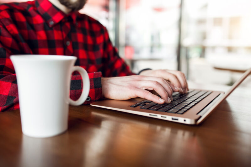 un barbat foloseste un laptop alaturi de care are o cana de cafea