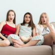 trei adolescente stau pe o canapea si se uita la un film