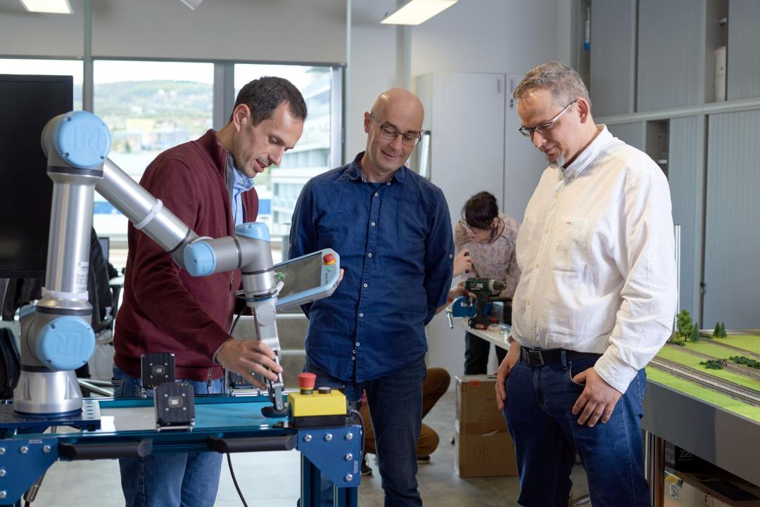 trei oameni in jurul unui brat robotic