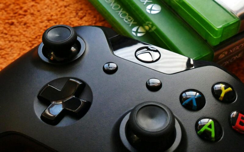 Xbox controller close-up with game cases on orange background.