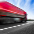 un camion rosu circula cu viteza pe un drum