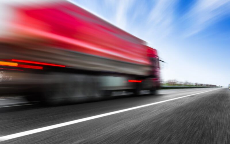 un camion rosu circula cu viteza pe un drum