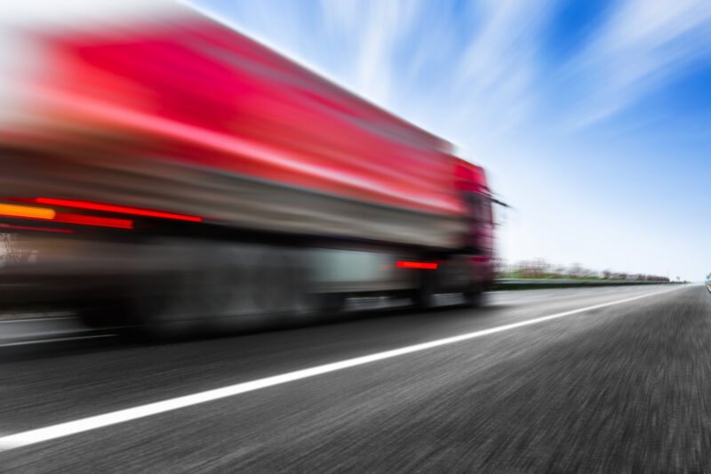 un camion rosu circula cu viteza pe un drum