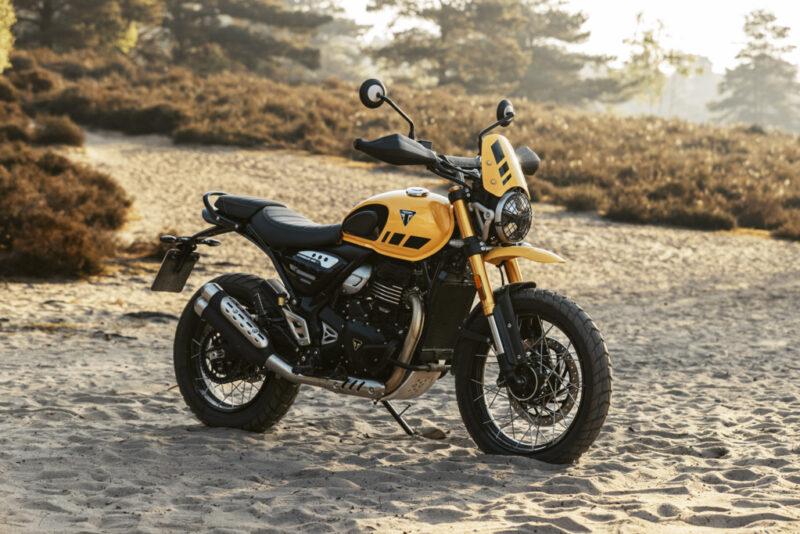 motocicleta galbena de tip scrambler adventure fotografiata la apus pe un teren accientat