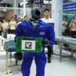 un robot industrial imbracat intr-o salopeta albastra tinand in maini o cutie verde