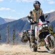 motocicleta de tip adventure fotografiata pe teren accidentat cu peisaj montan in spate