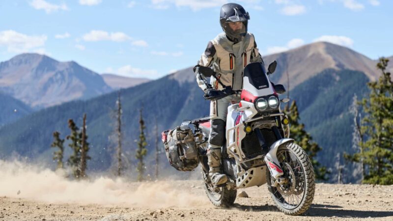 motocicleta de tip adventure fotografiata pe teren accidentat cu peisaj montan in spate