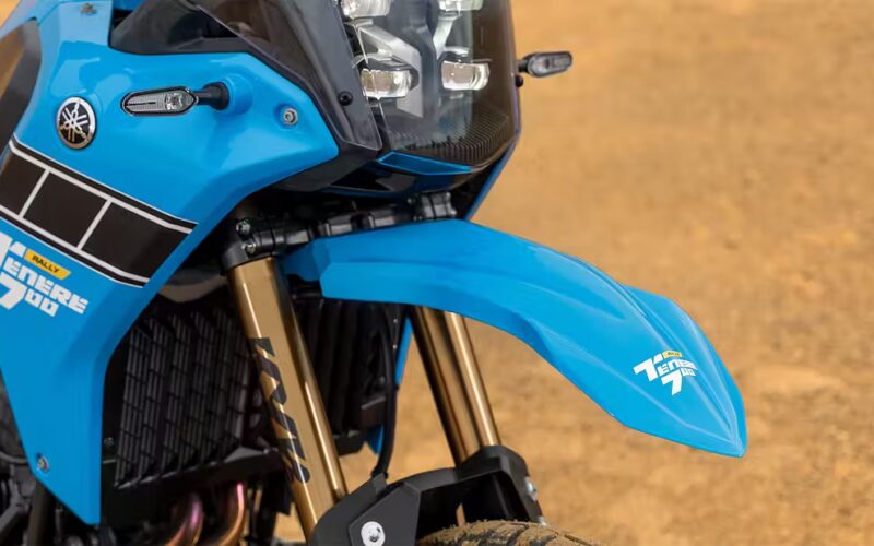 aripa fata si farul unei motociclete albastre cu un teren nisipos in fundal