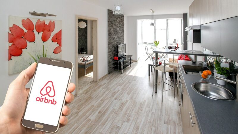 o mana care tine un telefon cu sigla AirBnb in interiorul unui apartament