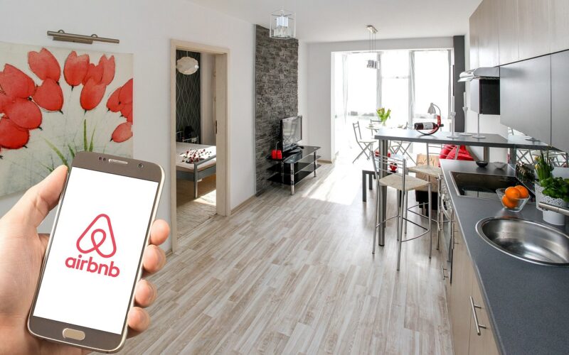 o mana care tine un telefon cu sigla AirBnb in interiorul unui apartament