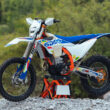 motocicleta enduro pe stand de culoare alb albastra la marginea unei paduri