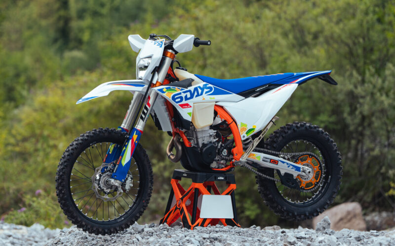 motocicleta enduro pe stand de culoare alb albastra la marginea unei paduri