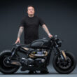 motocicleta custom made neagra alaturi de rider pe fundal negreu