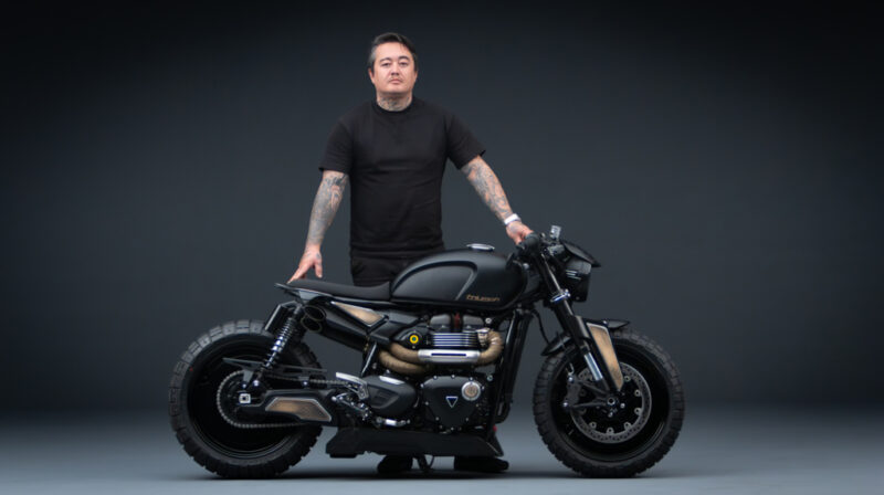 motocicleta custom made neagra alaturi de rider pe fundal negreu
