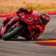 motocicleta rosie cu rider rosu inclinata pe partea dreapta pe un circuit de viteza