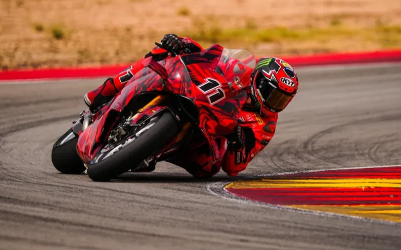 motocicleta rosie cu rider rosu inclinata pe partea dreapta pe un circuit de viteza