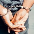 Prim-plan al mâinilor unui bărbat adult în cătușe, simbolizând aplicarea legii și justiția.