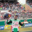 pilot de curse moto gp fotografiat cu casca si trofeul in mana cu multimea de fani in fundal