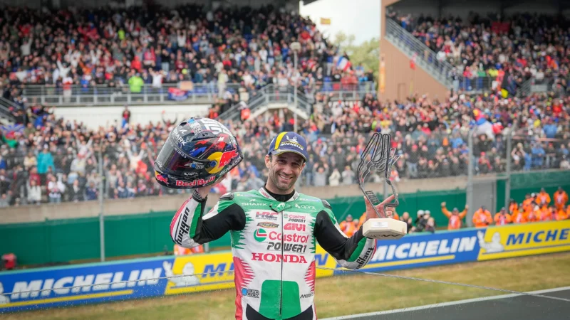 pilot de curse moto gp fotografiat cu casca si trofeul in mana cu multimea de fani in fundal