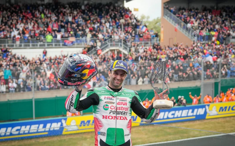 pilot de curse moto gp fotografiat cu casca si trofeul in mana cu multimea de fani in fundal