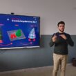 un om care vorbeste intr-o sala de clasa langa o tabla electronica