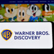 logo Warner Bros Discovery pe un telefon cu niste personaje de desene animate pe fundal