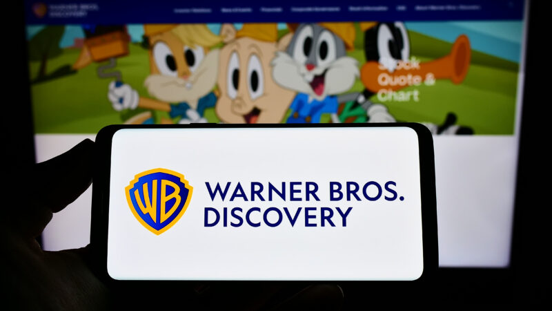 logo Warner Bros Discovery pe un telefon cu niste personaje de desene animate pe fundal