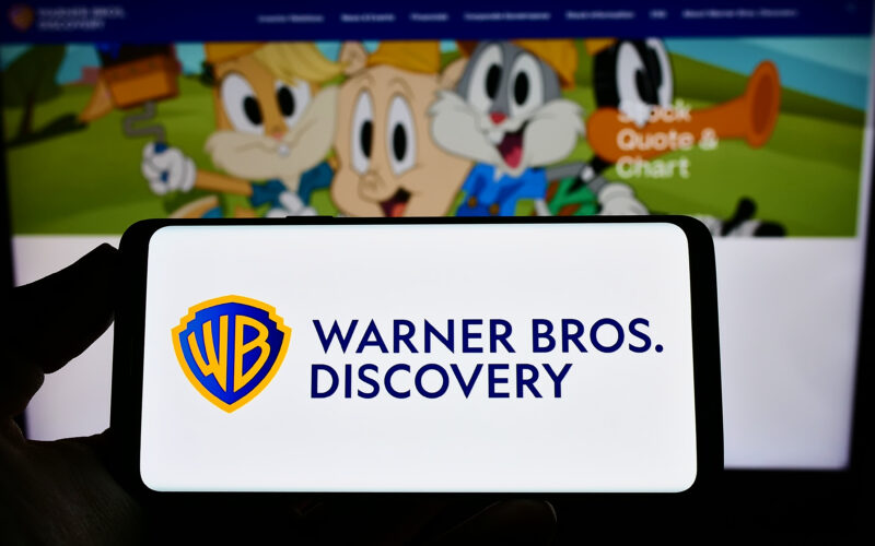 logo Warner Bros Discovery pe un telefon cu niste personaje de desene animate pe fundal