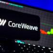 logo-ul companiei CoreWeave pe un telefon langa un ecran de laptop