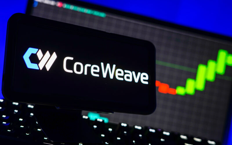 logo-ul companiei CoreWeave pe un telefon langa un ecran de laptop