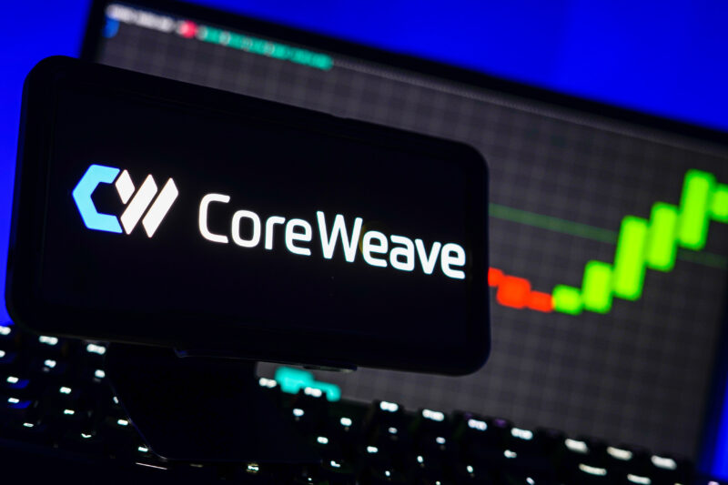 logo-ul companiei CoreWeave pe un telefon langa un ecran de laptop