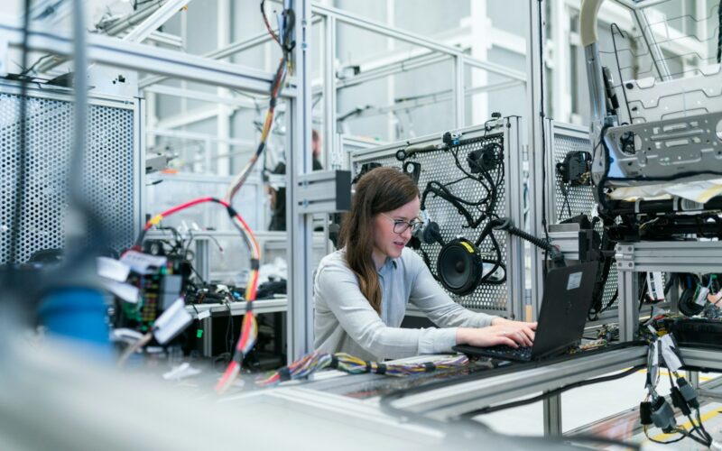 o femeie care lucreaza la un laptop intr-un mediu industrial